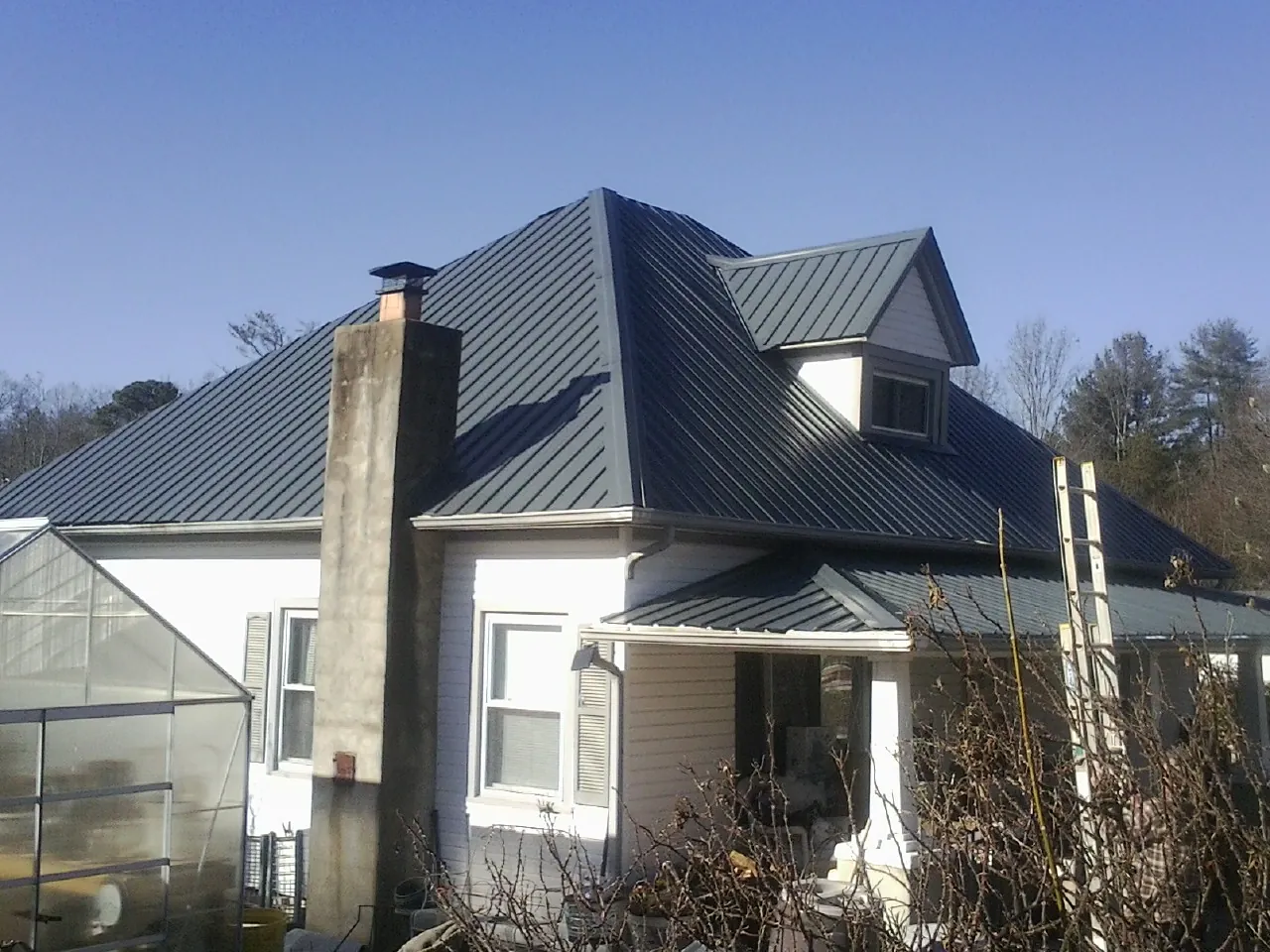 Dark blue standing seam metal roof on a white farmhouse with dormer — Slate & Tile Roof Repair by Roofing Brothers in Lennox