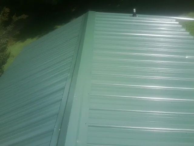 New green metal panels meeting at the ridge of a roof — Flat Roof Repair work by our crew in Lennox