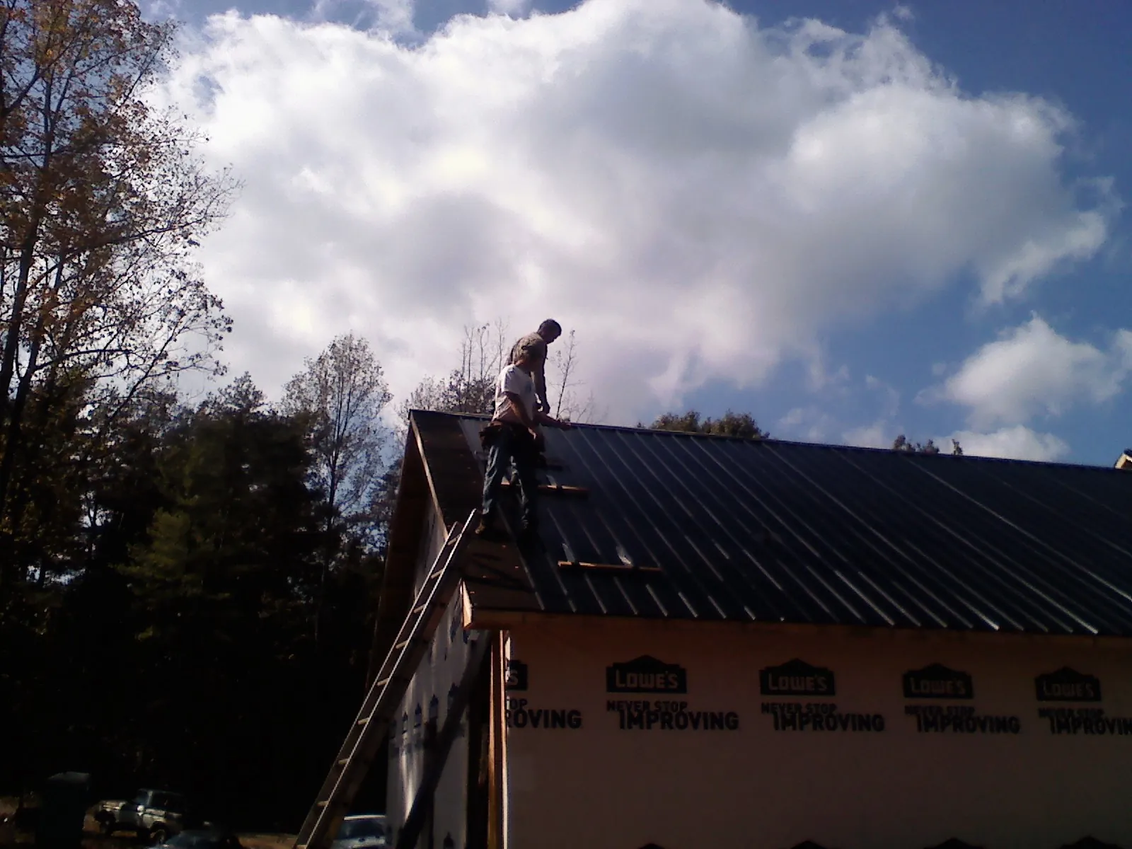 Roofer fastening dark metal panels high against a cloudy sky, from a Roof Inspection job in Lennox