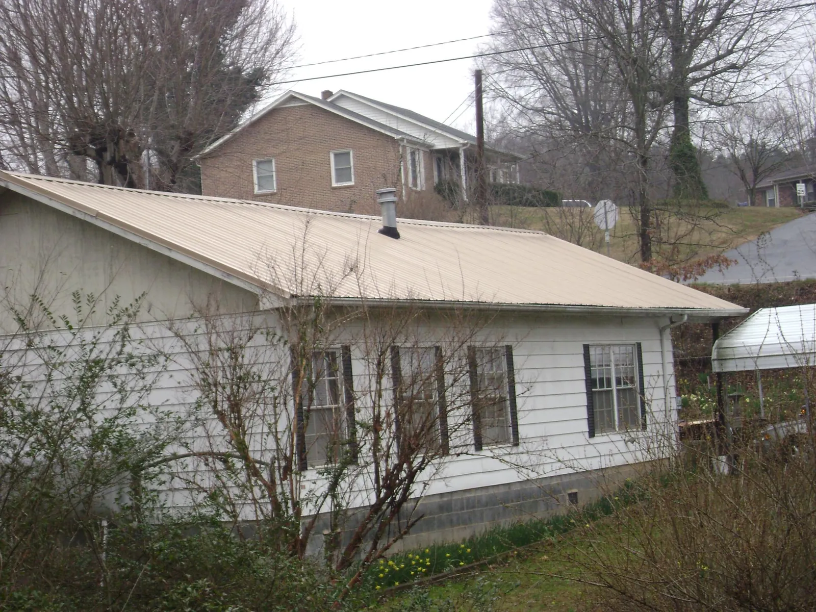 Tan metal roof on a white sided house set into a hillside — Commercial Roofing by Roofing Brothers in Lennox