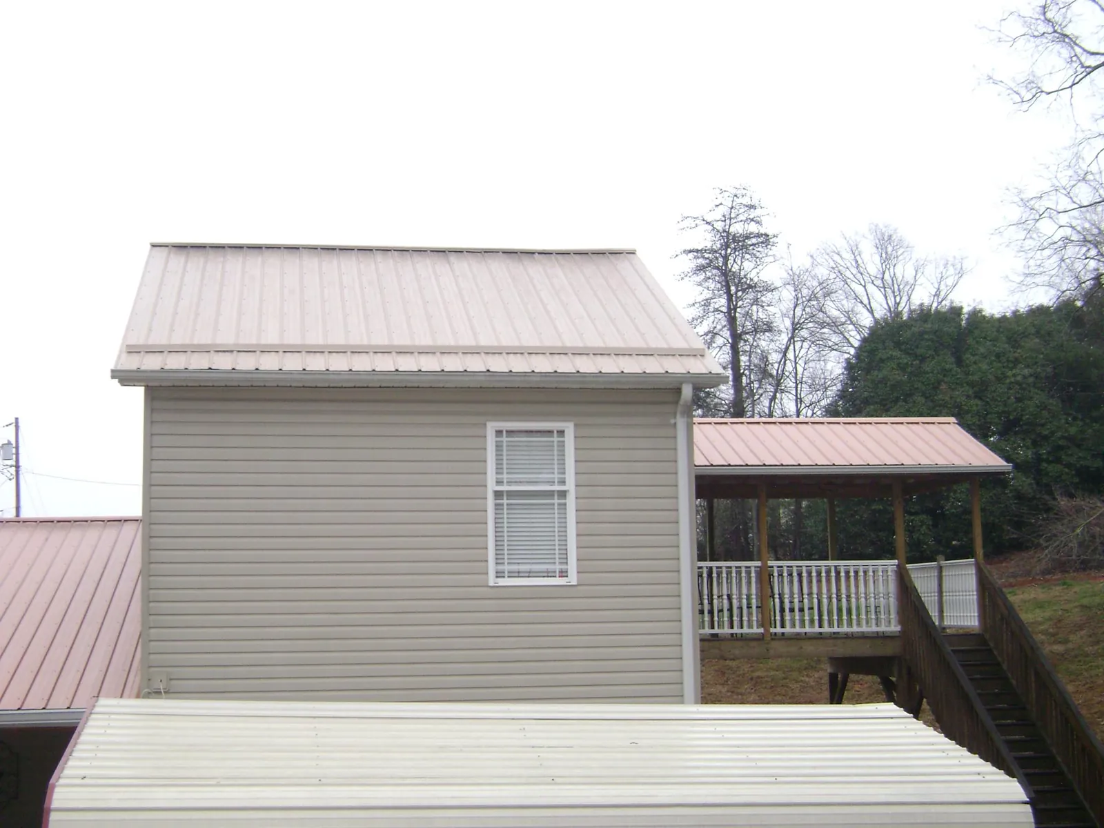 Tan metal roofs on a two story addition and attached porch, from a Roof Replacement job in Lennox